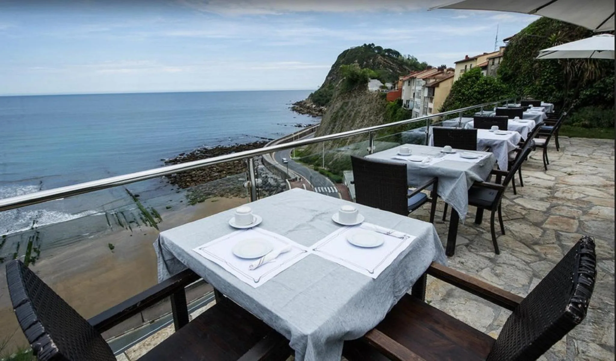 Tables dressées sur une terrasse surplombant la mer et la côte rocheuse.