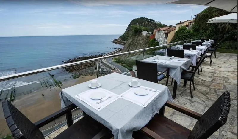 Tables dressées sur une terrasse surplombant la mer et la côte rocheuse.