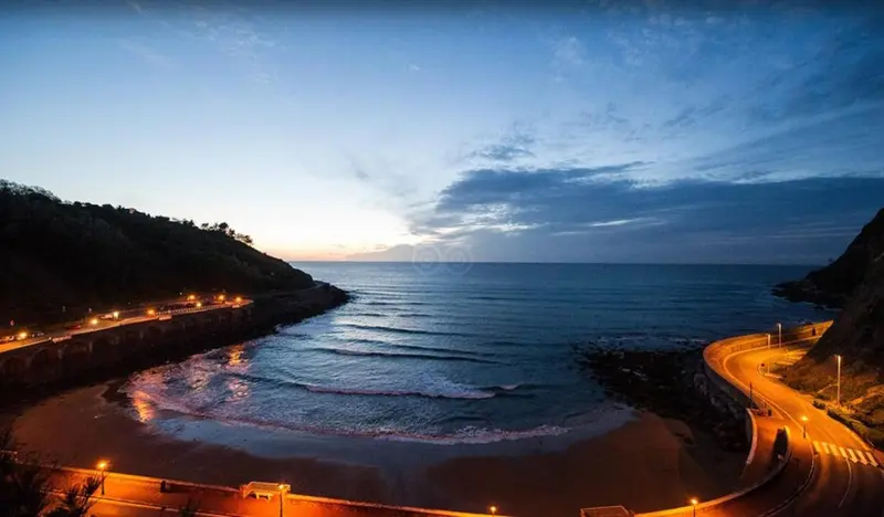 Vue panoramique sur une crique illuminée au crépuscule.