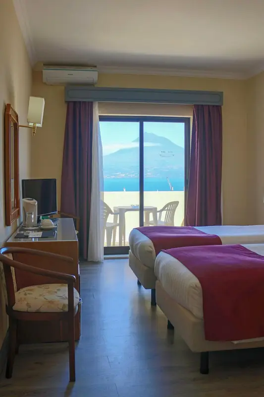 Une chambre lumineuse avec deux lits simples donnant sur une vue mer.