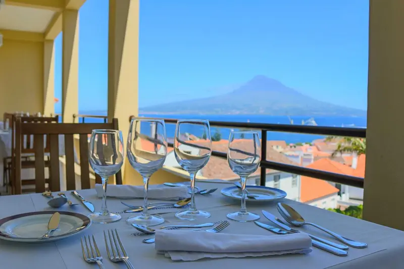 Une table dressée en extérieur offre une vue sur la mer et un volcan.