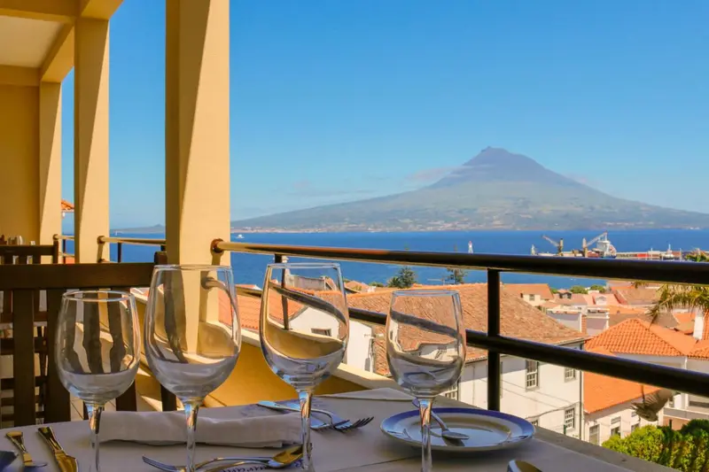 Une table dressée sur une terrasse offre une vue sur la mer et un volcan.