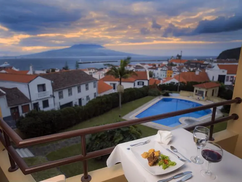 Une table est dressée sur un balcon avec vue sur la mer et un paysage urbain.