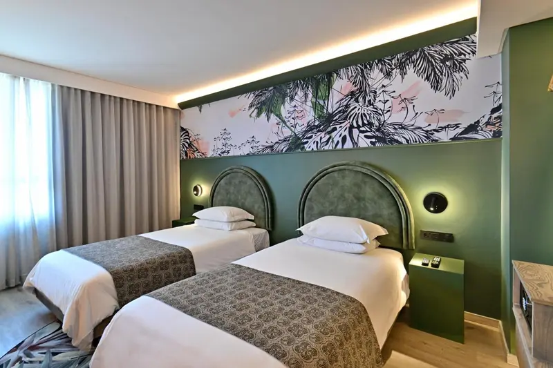 Une chambre avec deux lits simples et une décoration tropicale au mur.