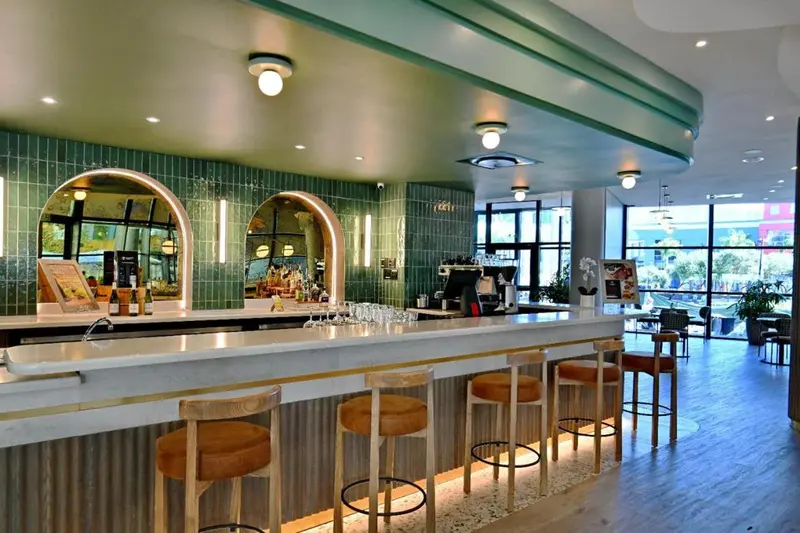 Un long comptoir de bar en marbre blanc avec des tabourets est éclairé par des luminaires suspendus.