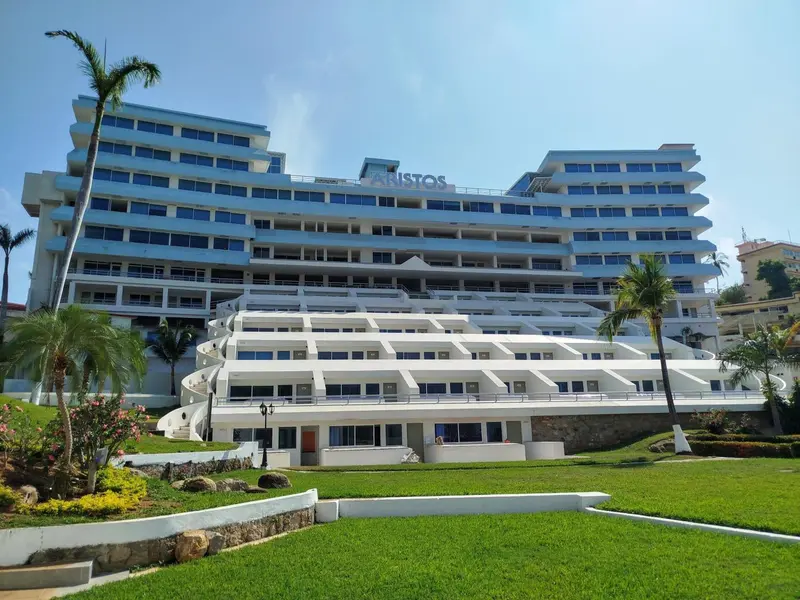 Bâtiment blanc à plusieurs étages avec des balcons surplombant une pelouse verdoyante.