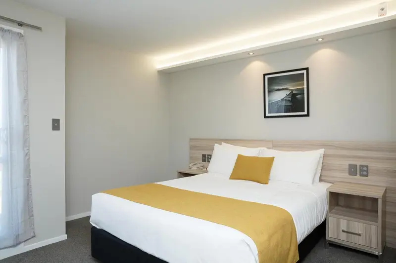 Une chambre lumineuse avec un lit recouvert d'une couverture jaune et d'oreillers blancs.