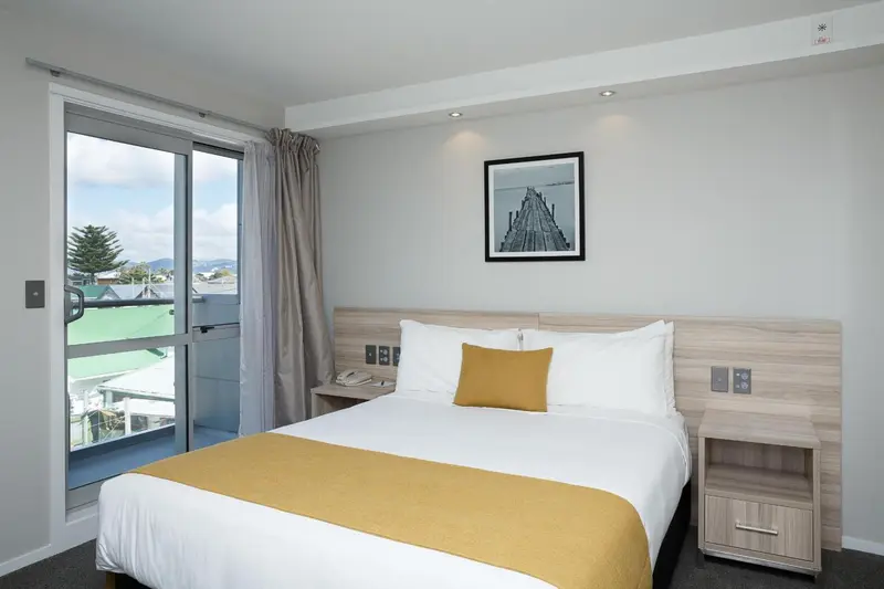 Chambre lumineuse avec un lit recouvert d'une couverture jaune et une vue sur la ville.