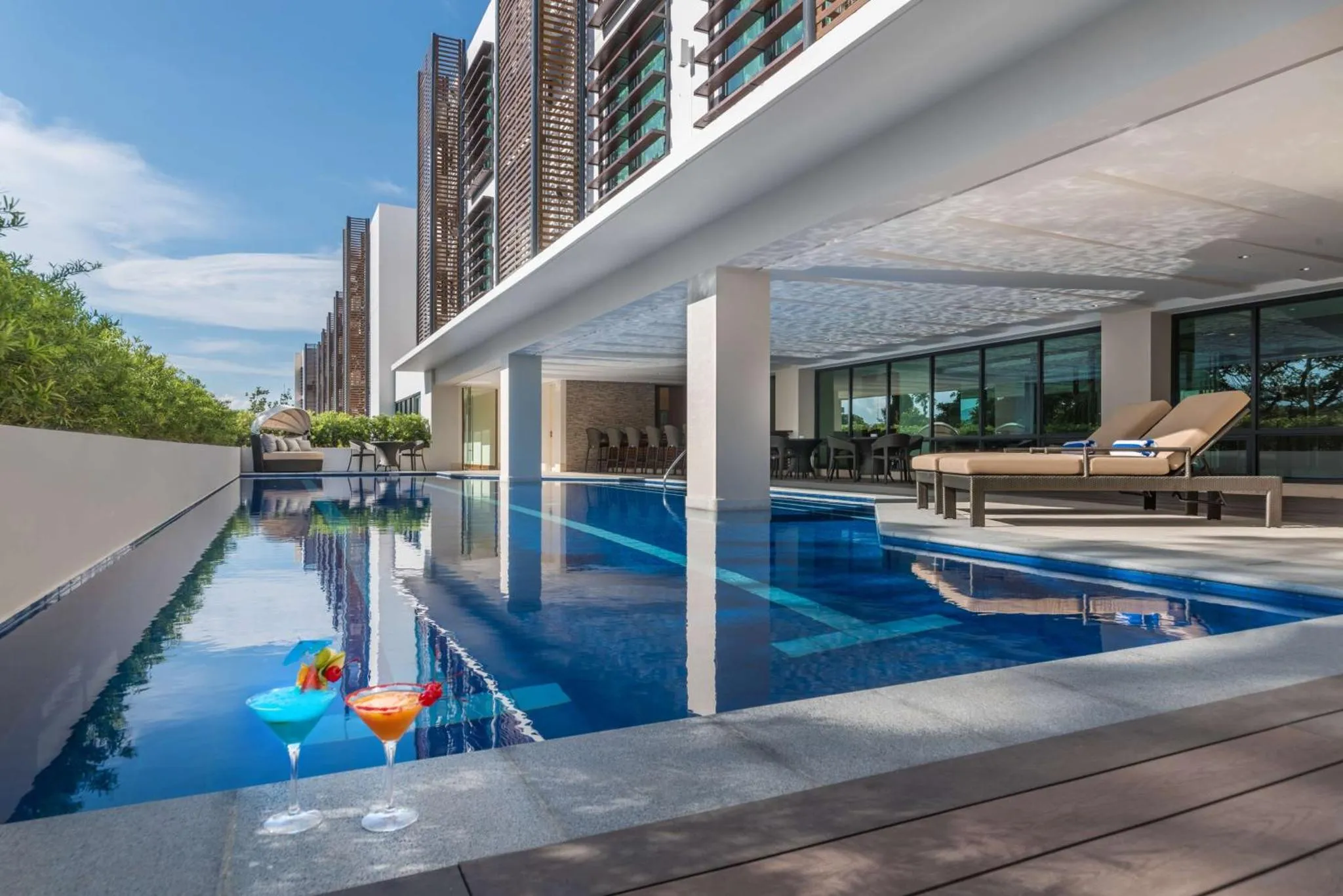 Deux cocktails colorés reposent sur le bord d'une piscine rectangulaire, avec des transats en arrière-plan.
