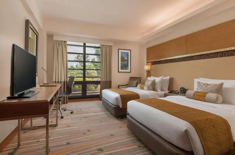Une chambre d'hôtel lumineuse avec deux lits et un bureau.