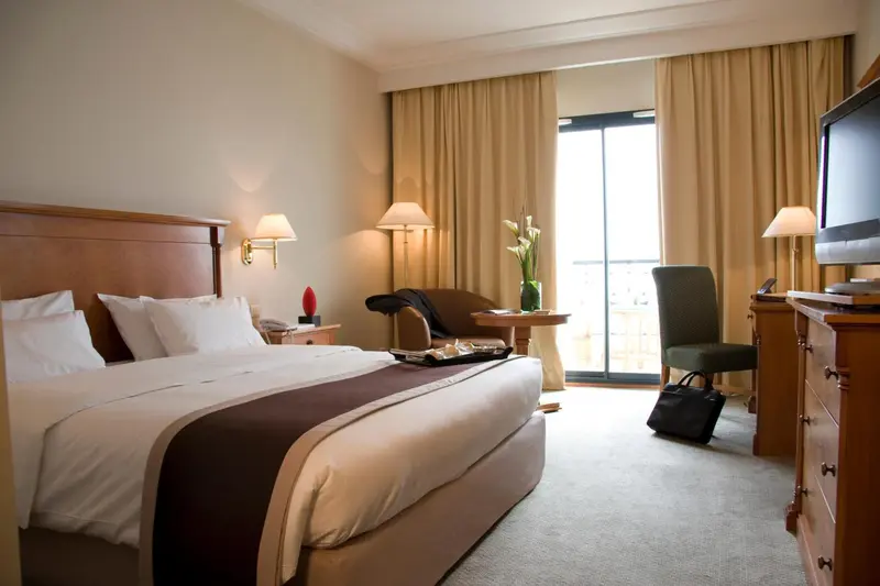 Une chambre lumineuse avec un grand lit et un coin salon près d'une baie vitrée.