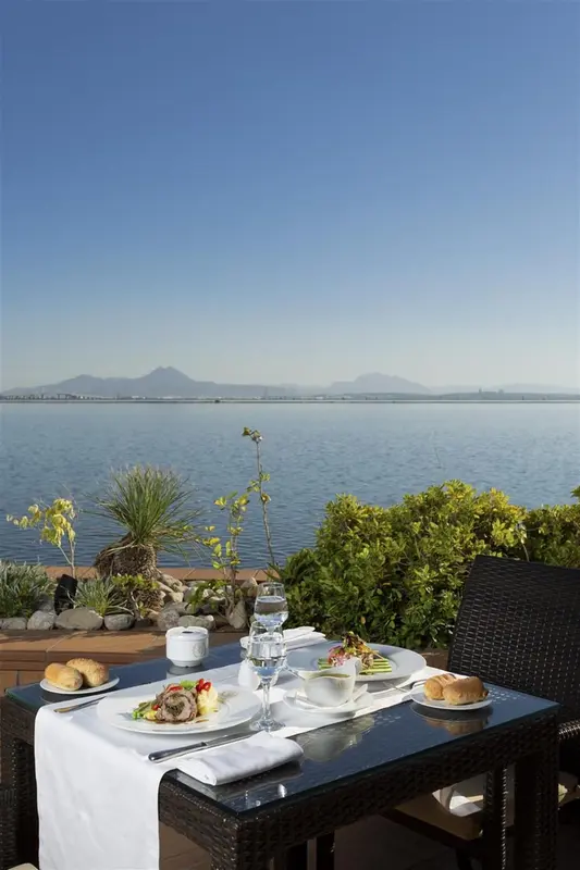 Une table est dressée pour un repas en extérieur avec vue sur la mer et les montagnes.