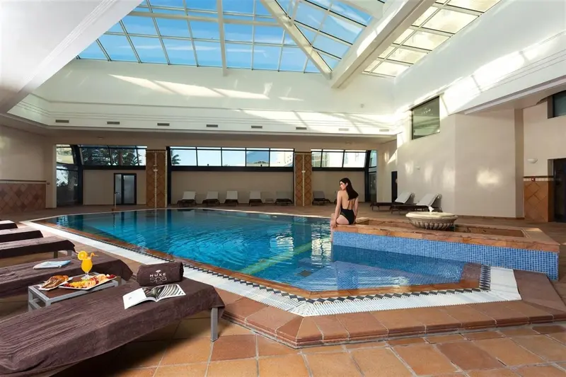 Une piscine intérieure lumineuse avec des transats et des boissons.