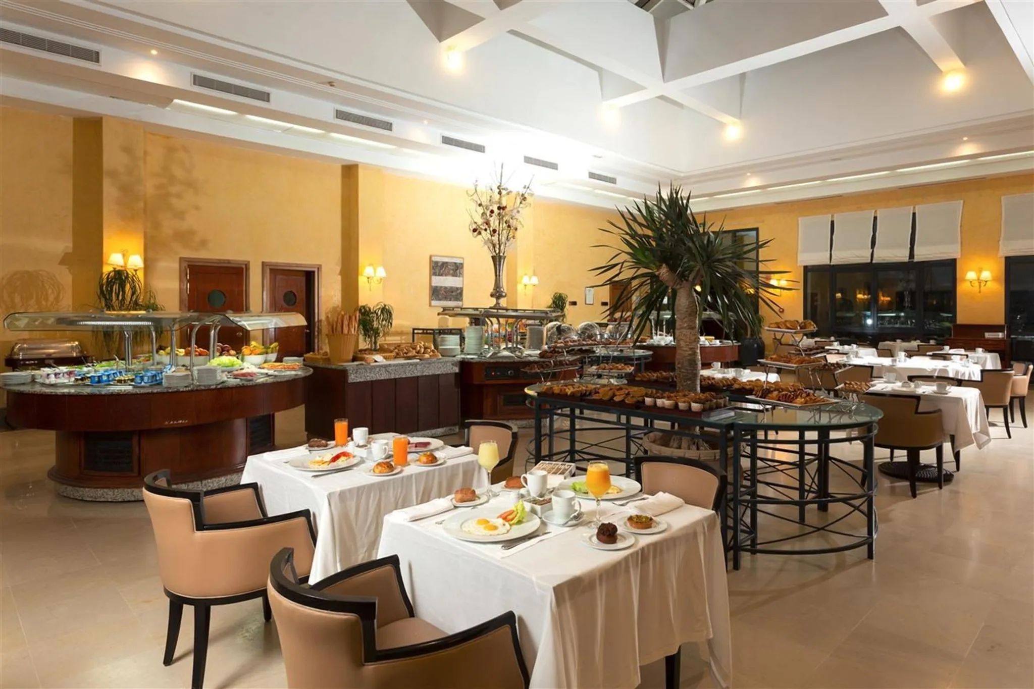 Une salle lumineuse présente un buffet garni de plats variés et des tables accueillent des clients pour le repas.