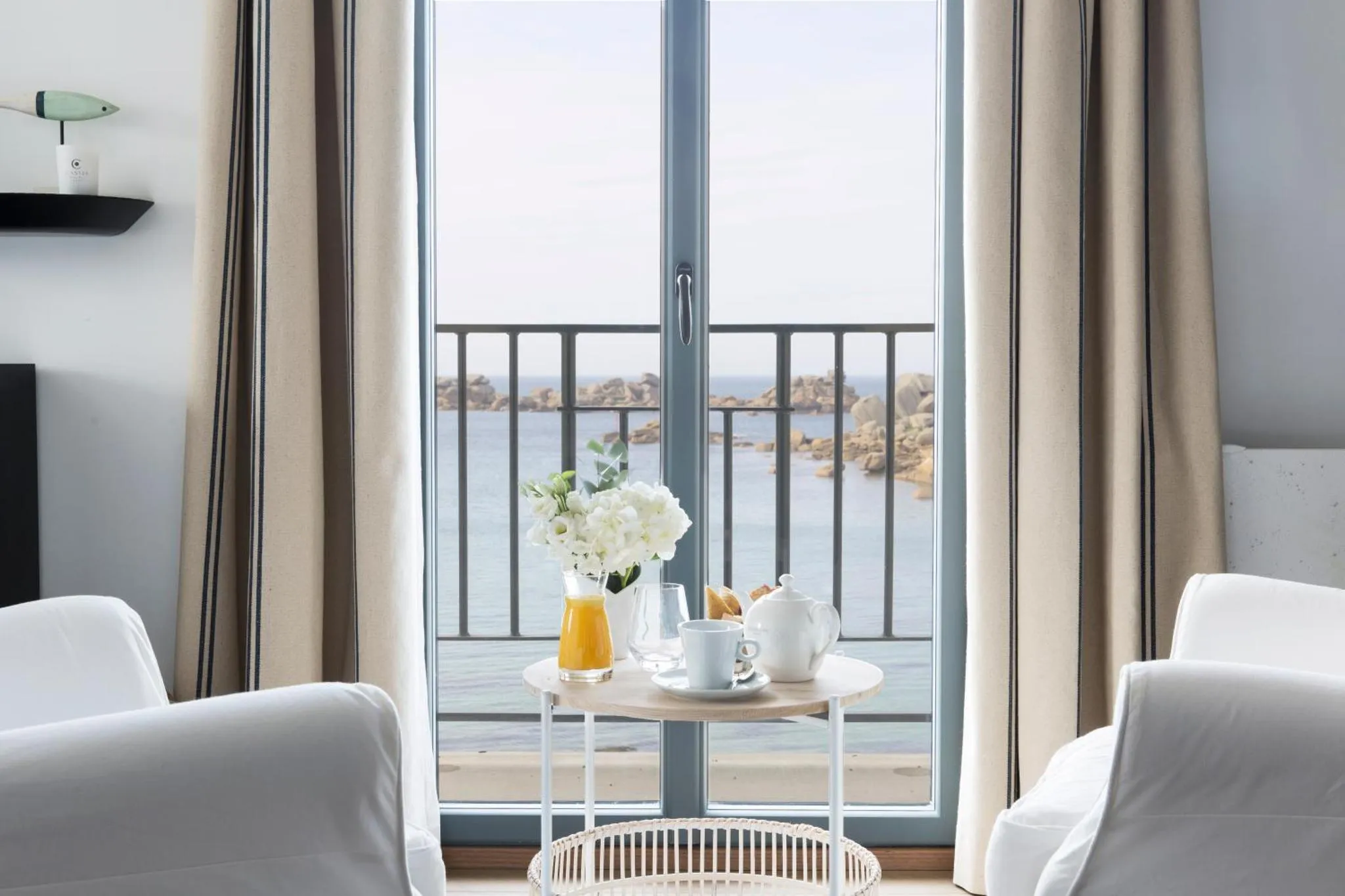 Une table ronde avec un petit-déjeuner est placée devant une baie vitrée donnant sur la mer.