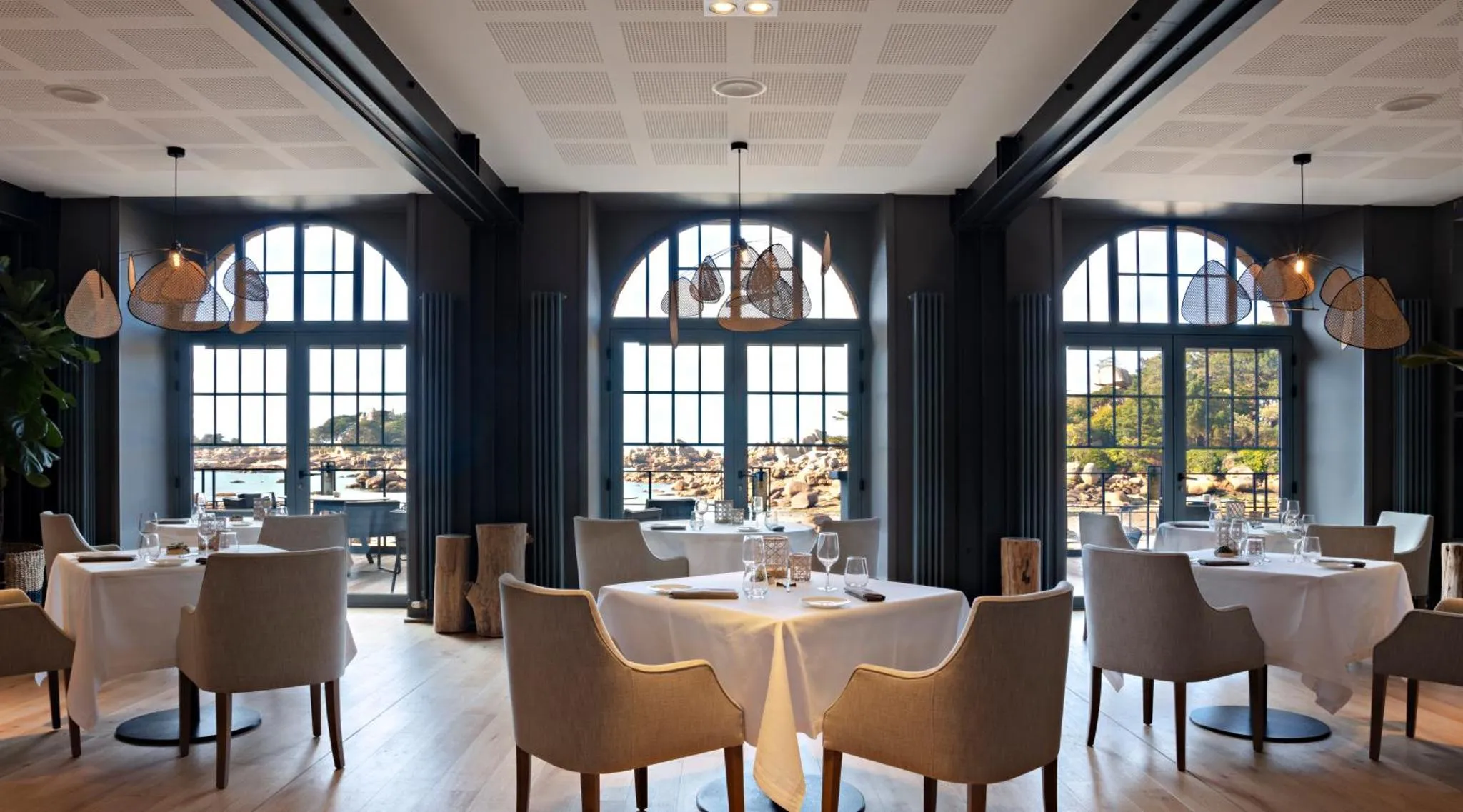 Une salle de restaurant lumineuse avec vue sur la mer par de grandes fenêtres.