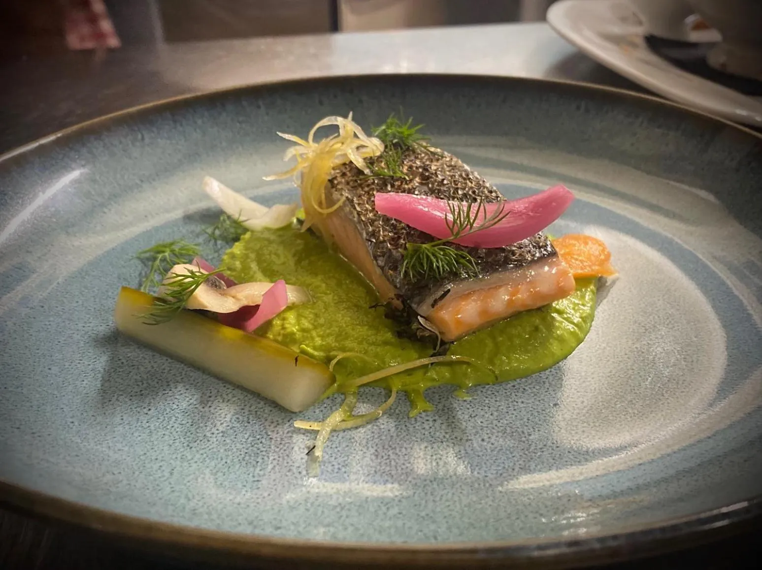 Assiette raffinée avec un morceau de poisson et une sauce verte.