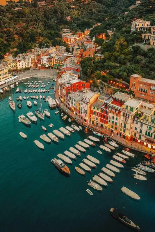 Vue aérienne d'un village coloré au bord de la mer, avec de nombreux bateaux amarrés dans un port.