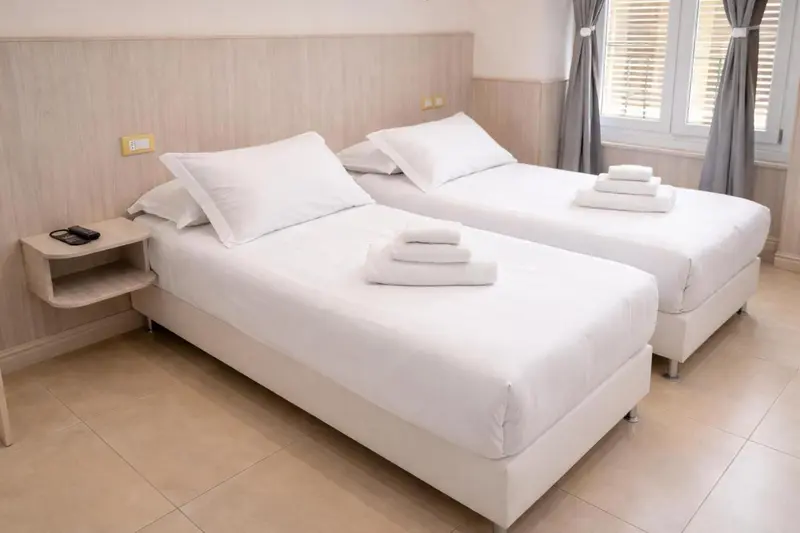 Deux lits simples avec linge blanc dans une chambre lumineuse.