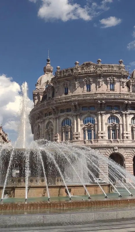 Fontaine monumentale jaillissant devant un bâtiment orné.