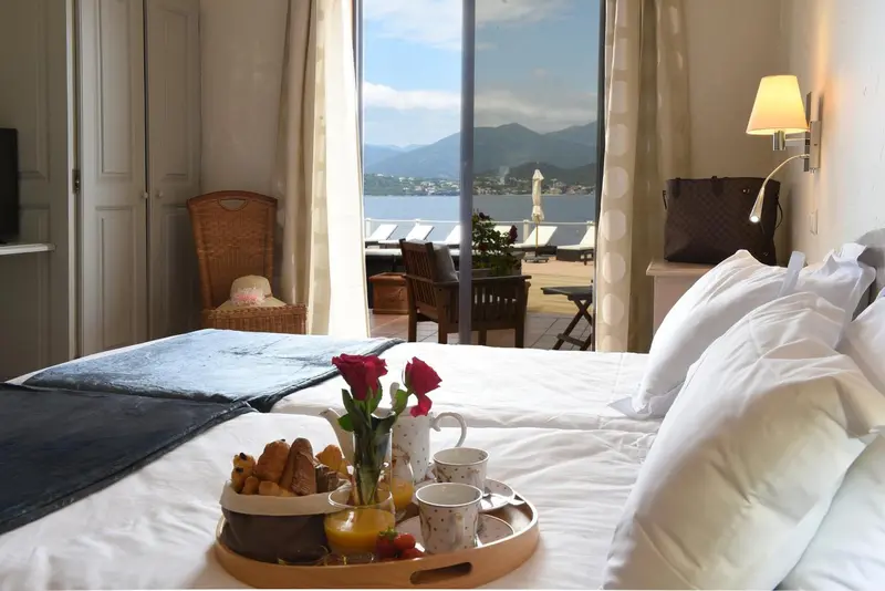 Une chambre avec un lit preparé pour le petit-déjeuner, donnant sur une terrasse et la mer.