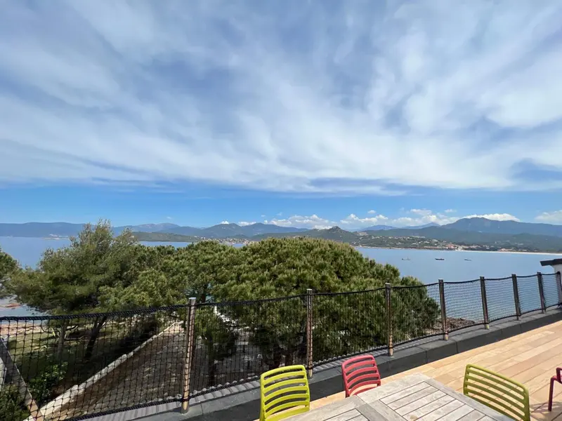Vue panoramique sur la mer et les montagnes depuis une terrasse ensoleillée.