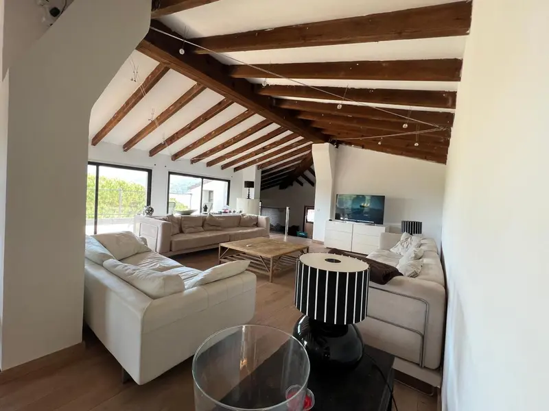 Un salon spacieux avec canapés clairs et plafond en bois apparent.