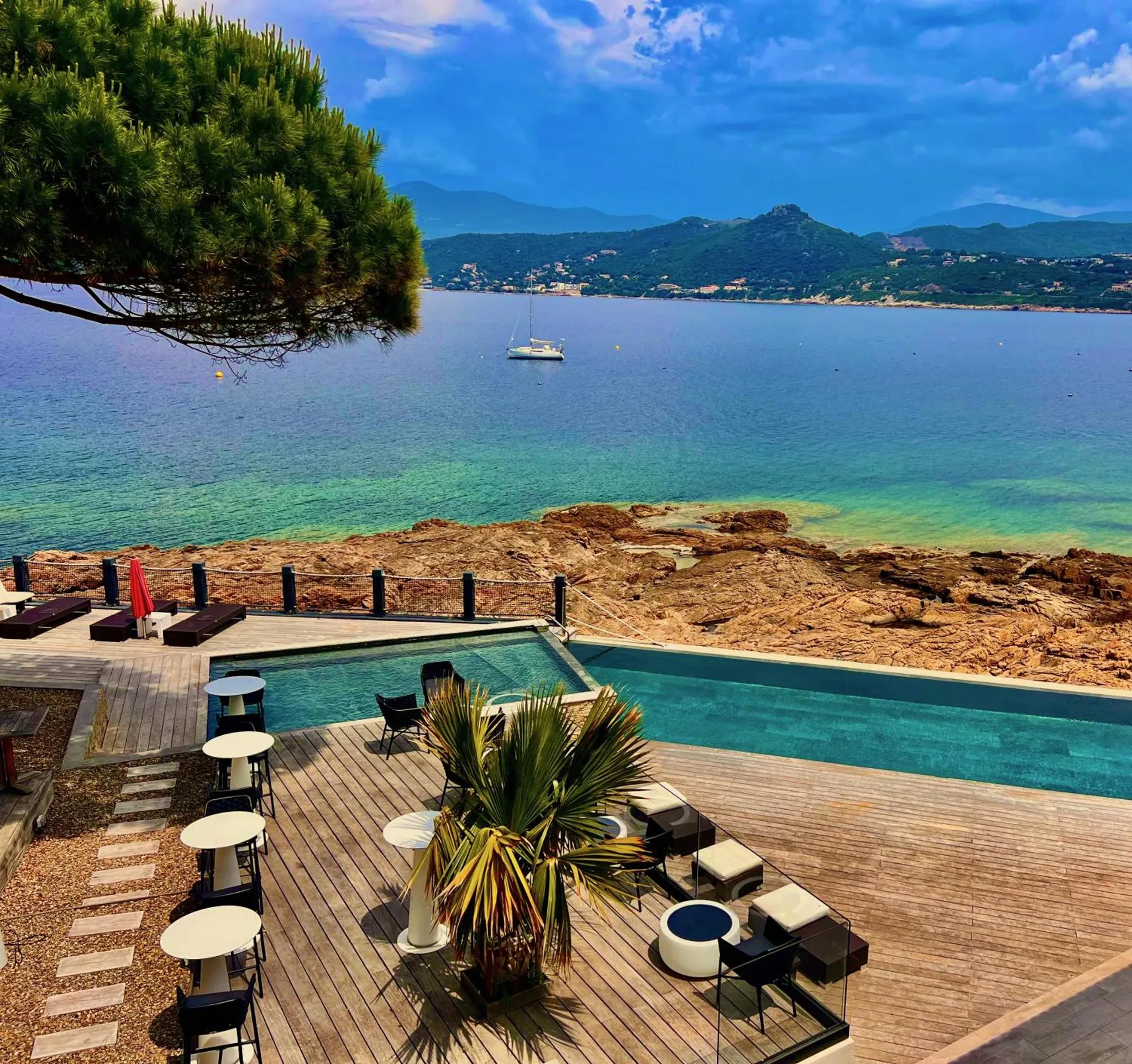 Terrasse avec transats et piscine à débordement surplombant la mer.