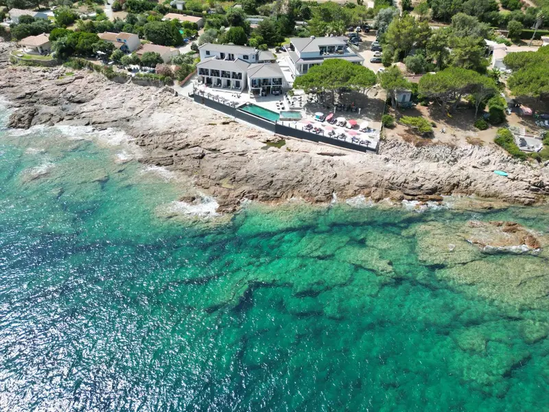 Vue aérienne d'un établissement au bord de mer avec piscine et végétation luxuriante.