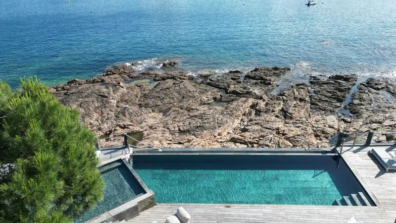 Une piscine à débordement surplombe une côte rocheuse et la mer.