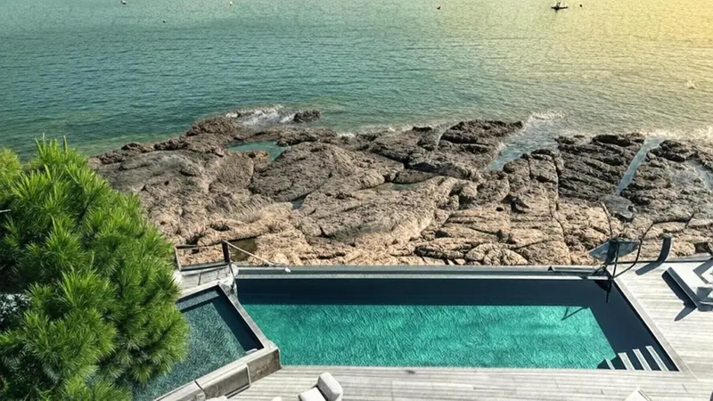 Une piscine à débordement surplombe une côte rocheuse et la mer.