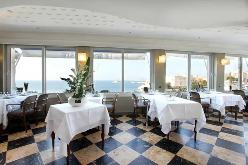 Une salle lumineuse avec des tables dressées face à une vue sur la mer.
