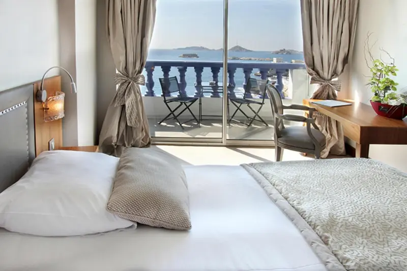 Une chambre lumineuse avec un grand lit donnant sur une terrasse et une vue sur la mer.