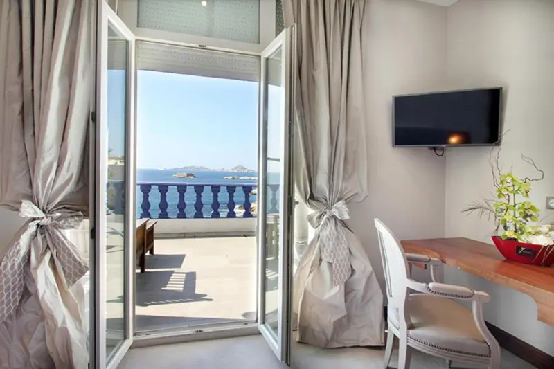 Une chambre lumineuse s'ouvre sur un balcon avec vue sur la mer.
