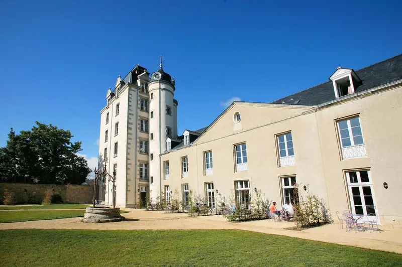 Facade d'un bâtiment ancien avec un jardin verdoyant devant.