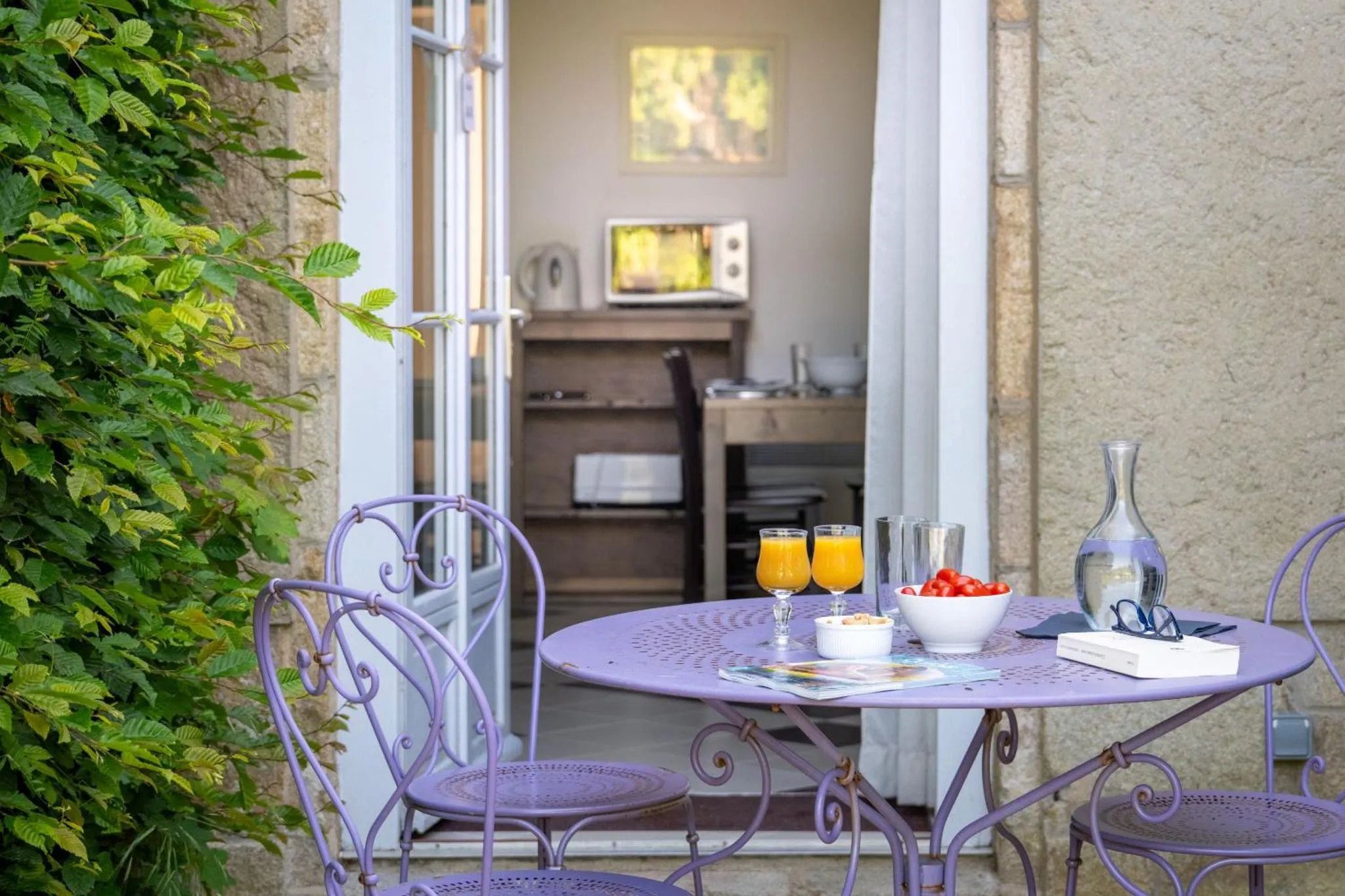 Une table ronde avec des verres de jus d'orange et des fruits est mise en scène devant une cuisine.