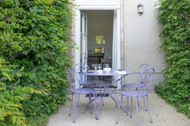 Une table et des chaises violettes sont disposées devant une porte ouverte sur une cuisine.