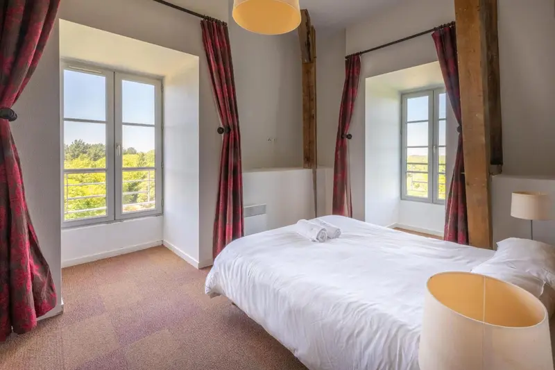 Une chambre lumineuse avec un lit recouvert d'une courtepointe blanche et deux fenêtres.