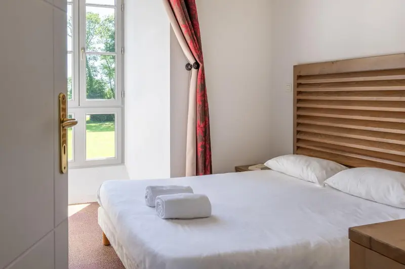 Une chambre lumineuse avec un lit double et une vue sur un jardin.