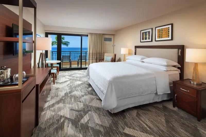 Chambre lumineuse avec un grand lit et une vue sur la mer par une baie vitrée.