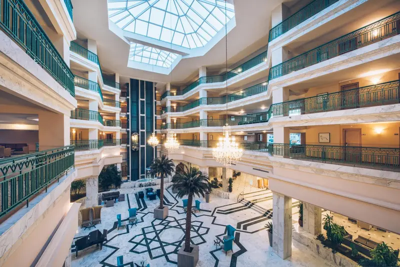 Vue intérieure d'un hall d'hôtel avec une verrière et des palmiers.