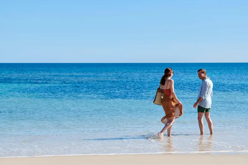 Un couple marche sur une plage de sable clair au bord d'une mer turquoise.
