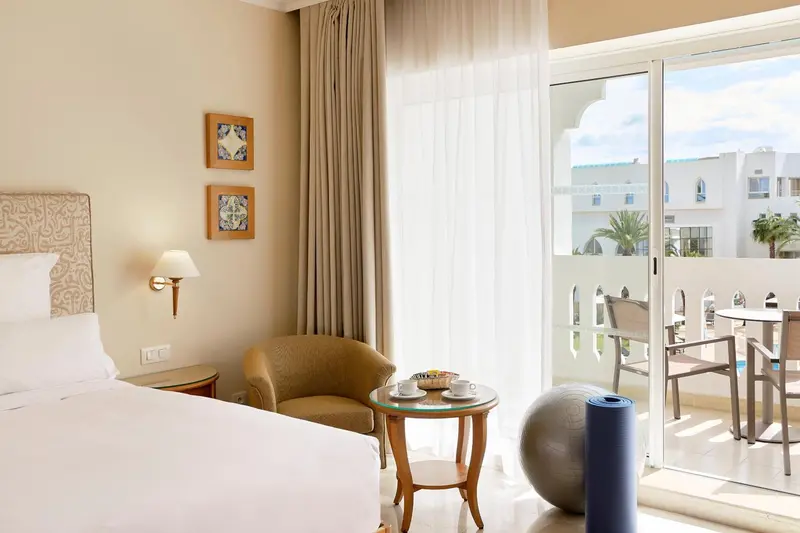 Une chambre lumineuse avec un lit, un fauteuil et un accès à une terrasse.