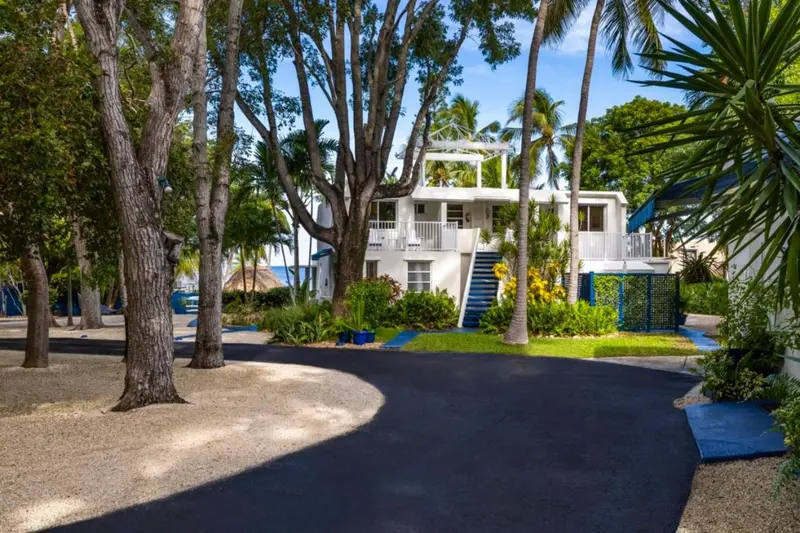 Bâtiment blanc à deux étages entouré de végétation tropicale et d'une allée sombre.