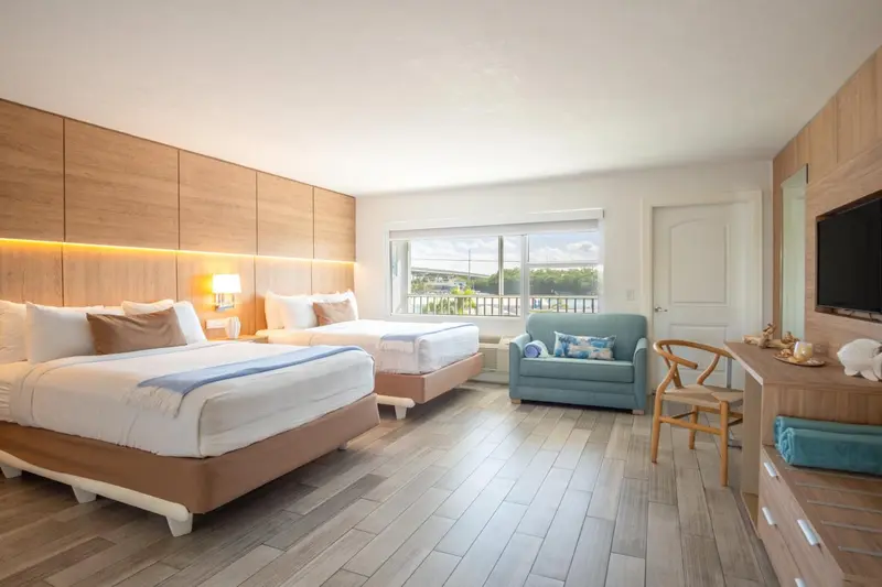 Chambre lumineuse avec deux lits et un coin salon près d'une fenêtre.