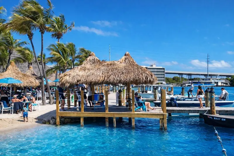 Terrasse ombragée avec tables et chaises au bord de l'eau turquoise.