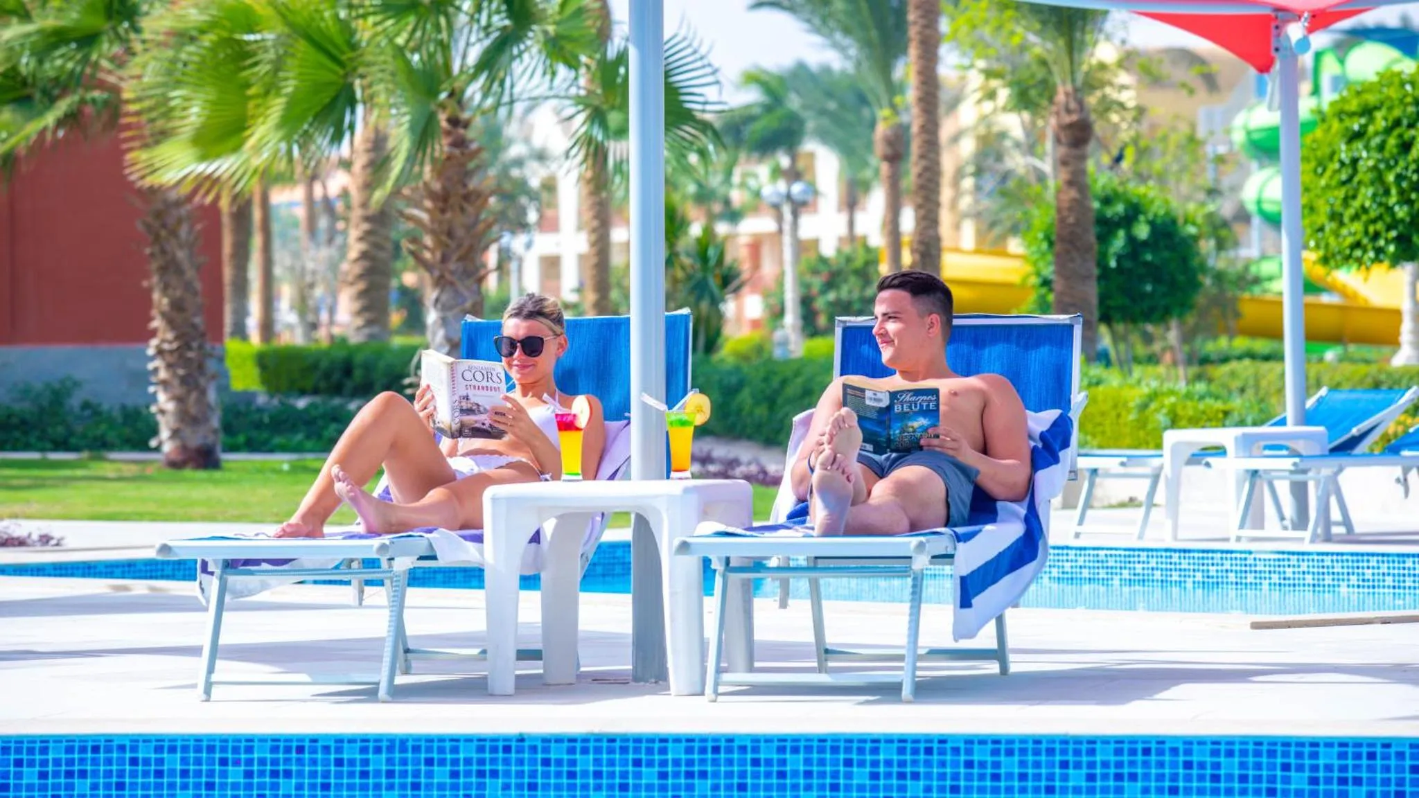 Deux personnes se relaxent sur des transats près d'une piscine ensoleillée.