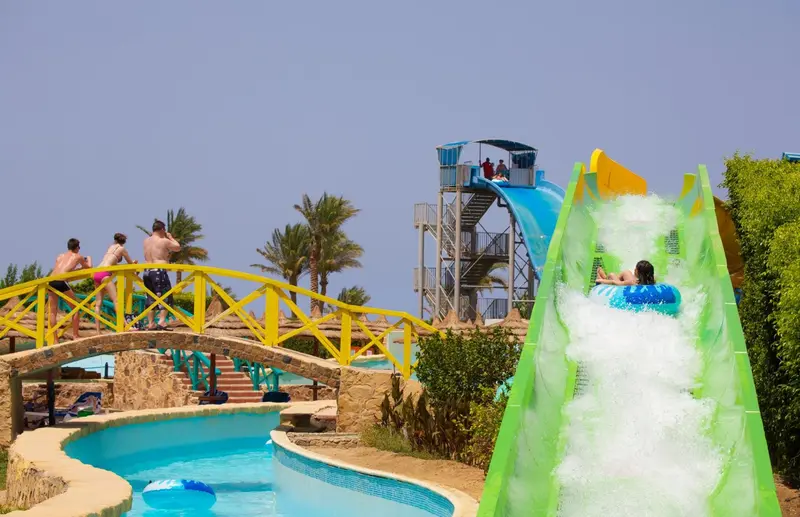Un toboggan aquatique vert se termine dans une piscine bleue.