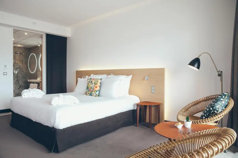 Une chambre lumineuse avec un grand lit et un fauteuil en rotin.