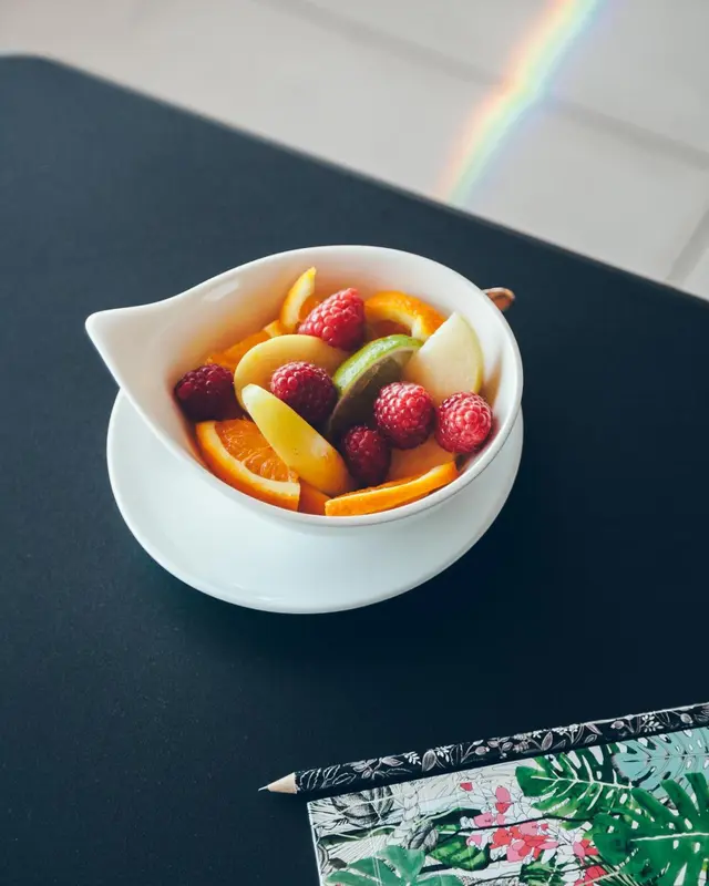 Une salade de fruits frais est présentée dans un bol blanc sur une table sombre.